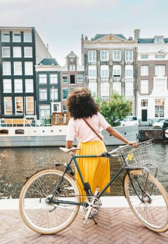 Photo shows a young woman on a bicycle by a canal in Amsterdam, Netherlands. Amsterdam just became the first capital city in the world to ban ads for meat and fossil fuel related products in public spaces
