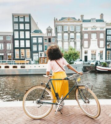 Photo shows a young woman on a bicycle by a canal in Amsterdam, Netherlands. Amsterdam just became the first capital city in the world to ban ads for meat and fossil fuel related products in public spaces