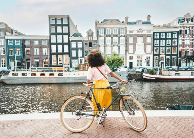 Photo shows a young woman on a bicycle by a canal in Amsterdam, Netherlands. Amsterdam just became the first capital city in the world to ban ads for meat and fossil fuel related products in public spaces