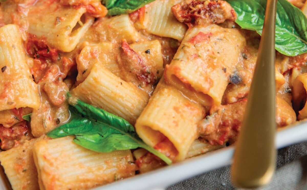a baked hummus pasta dish with hummus, sun-dried tomatoes, tomato, rigatoni, and basil for affordable and easy vegan recipes