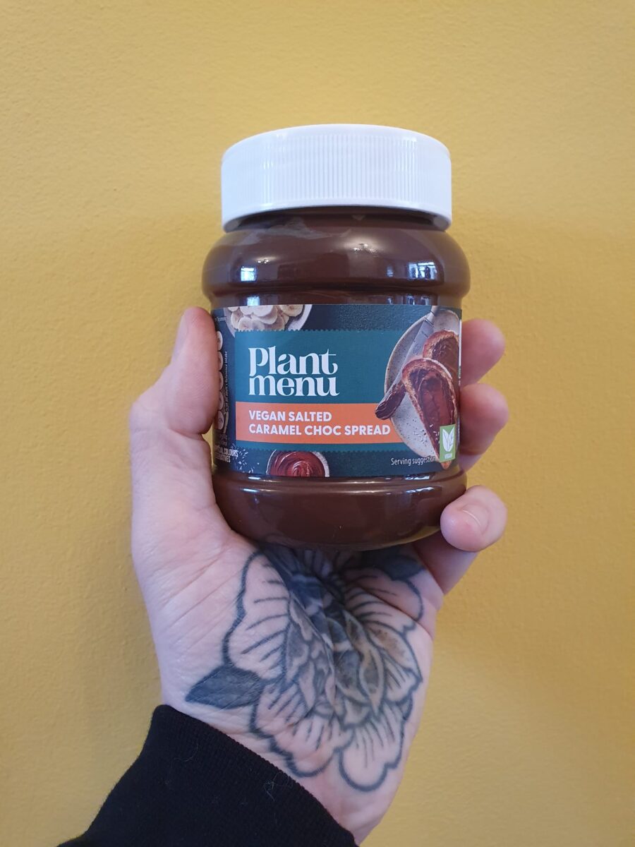 Photo shows someone's hand holding up a jar of Aldi's Plant Menu salted caramel chocolate spread, new for Veganuary 2026