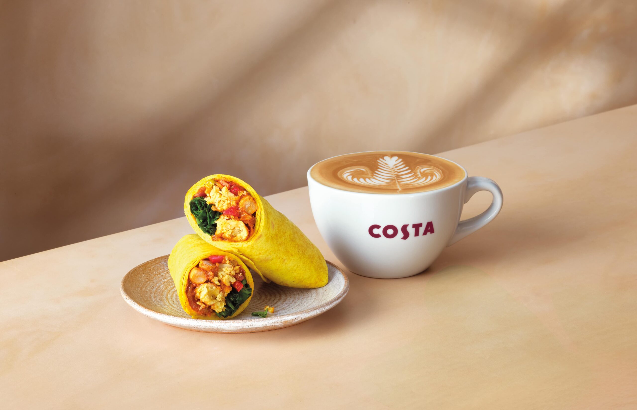 Photo shows a latte in a Costa cup next to the new Vegan Onion Bhaji Wrap, which Costa Coffee has introduced for Veganuary