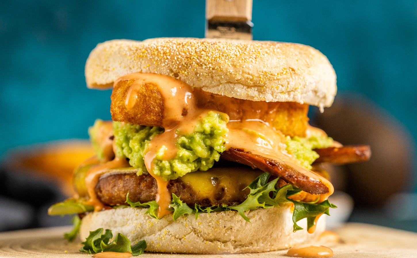 a picture of a stacked vegan breakfast burger made with vegan burger patties, vegan smoky bacon, vegan cheddar, guacamole, and more topped on an English muffin for cozy vegan breakfasts