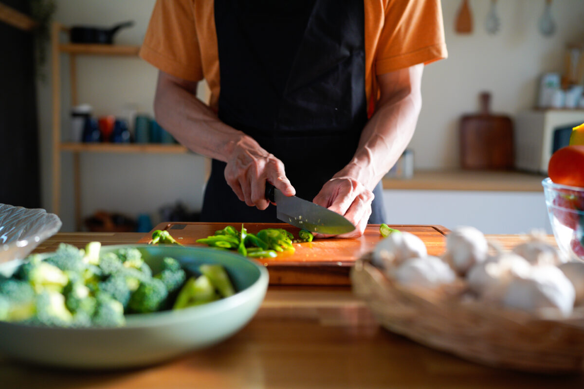 Photo shows someones hands as they chop and prepare vegetables on a wooden board