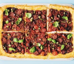a picture of six squares of a caramelized shallot and tomato tart topped with basil and capers for vegan savory tart ideas for both sweet and savory recipes