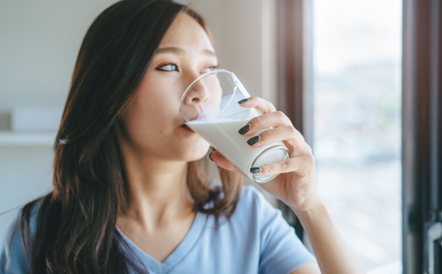 Photo shows a young woman drinking milk while looking out of her kitchen window. New research by Danone and INNOFACT has found that nearly half of German adults now drink plant-based milk alternatives