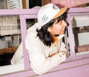 Photo shows a barista wearing the new Oatly x KOI cap. Oatly and Kids of Immigrants (KOI), an LA-based fashion brand, just launched a new limited-edition workwear capsule inspired by baristas.