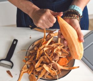 Woman peeling a raw sweet potato to illustrate article about which fruits and vegetables to peel