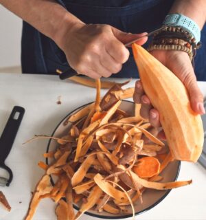 Woman peeling a raw sweet potato to illustrate article about which fruits and vegetables to peel