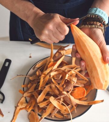 Woman peeling a raw sweet potato to illustrate article about which fruits and vegetables to peel