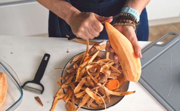 Woman peeling a raw sweet potato to illustrate article about which fruits and vegetables to peel