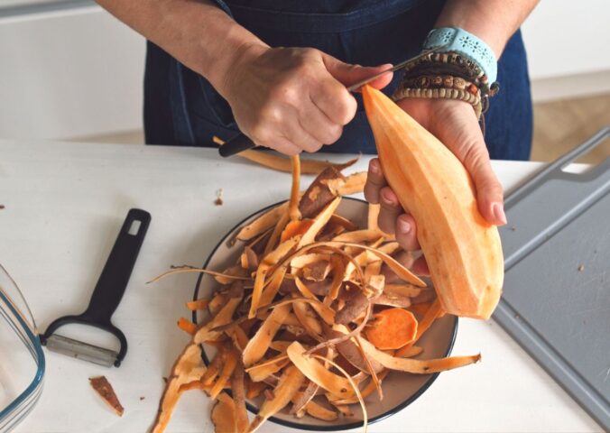 Woman peeling a raw sweet potato to illustrate article about which fruits and vegetables to peel