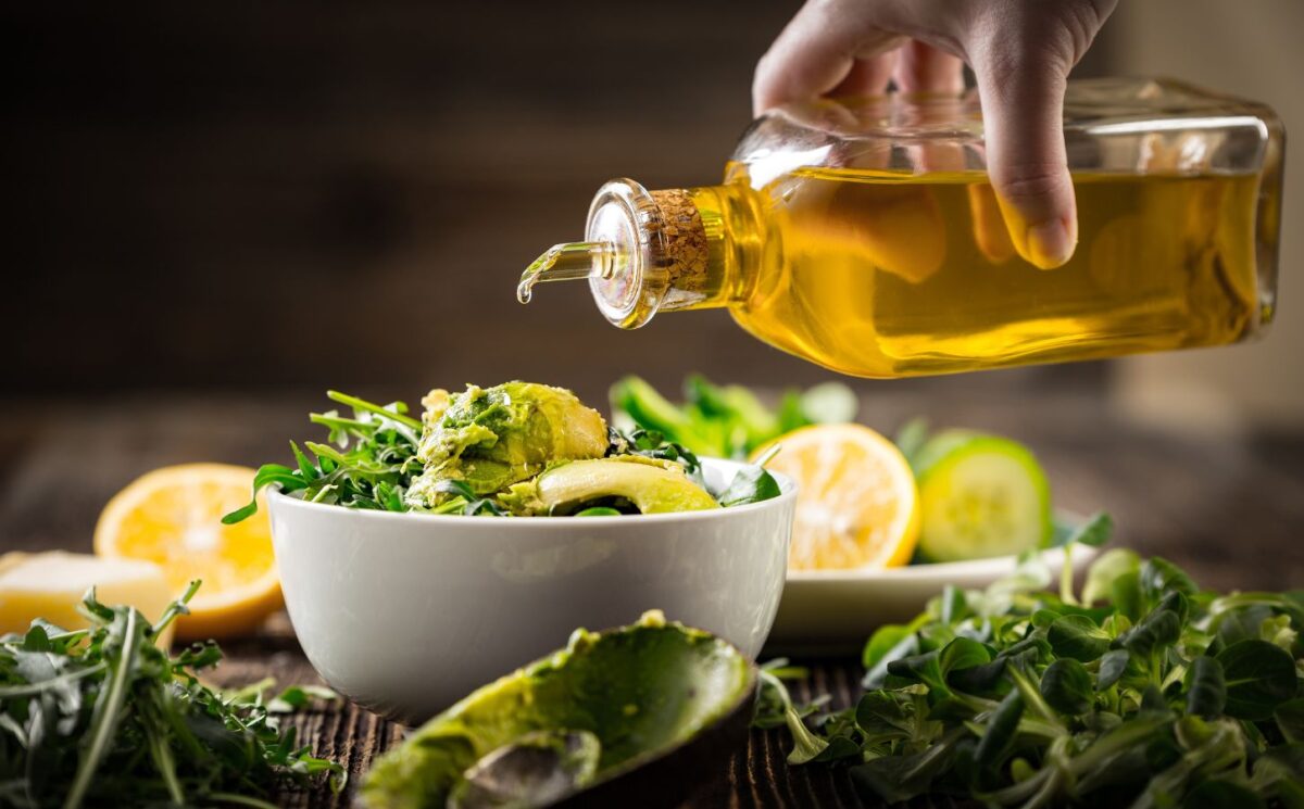 Shot of hand pouring olive oil onto salad bowl to illustrate article exploring the low fat vegan diet