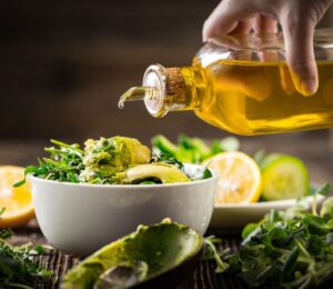 Shot of hand pouring olive oil onto salad bowl to illustrate article exploring the low fat vegan diet