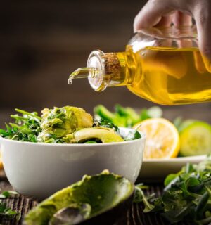 Shot of hand pouring olive oil onto salad bowl to illustrate article exploring the low fat vegan diet