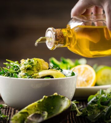 Shot of hand pouring olive oil onto salad bowl to illustrate article exploring the low fat vegan diet