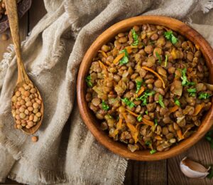 Cooked green lentils with carrot and onion in wooden bowl to illustrate article about the lentil that beats the rest