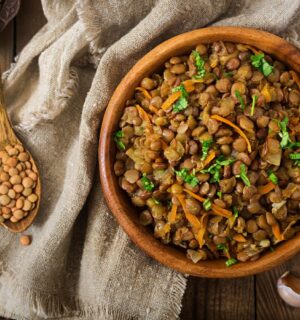 Cooked green lentils with carrot and onion in wooden bowl to illustrate article about the lentil that beats the rest