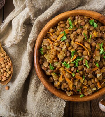 Cooked green lentils with carrot and onion in wooden bowl to illustrate article about the lentil that beats the rest