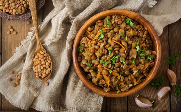 Cooked green lentils with carrot and onion in wooden bowl to illustrate article about the lentil that beats the rest
