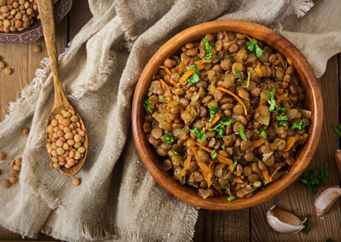 Cooked green lentils with carrot and onion in wooden bowl to illustrate article about the lentil that beats the rest