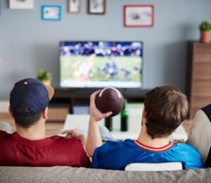 Photo shows three men on a sofa facing away from the camera and watching American football. According to a new survey, many Americans will be eating chicken wings during this Sunday's Super Bowl, and most of them would consider a plant-based or vegan alternative