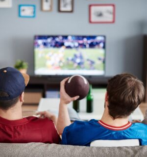 Photo shows three men on a sofa facing away from the camera and watching American football. According to a new survey, many Americans will be eating chicken wings during this Sunday's Super Bowl, and most of them would consider a plant-based or vegan alternative