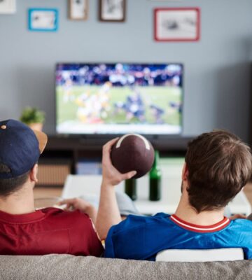 Photo shows three men on a sofa facing away from the camera and watching American football. According to a new survey, many Americans will be eating chicken wings during this Sunday's Super Bowl, and most of them would consider a plant-based or vegan alternative