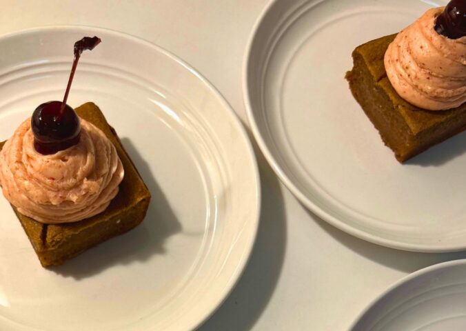 a photo of banana split butter mochi with strawberry buttercream and cherries