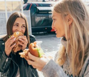 Photo shows two women laughing and eating lunch in an outdoor restaurant area with foodtrucks. London was recently named the best vegan city in the UK and in the world