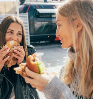 Photo shows two women laughing and eating lunch in an outdoor restaurant area with foodtrucks. London was recently named the best vegan city in the UK and in the world
