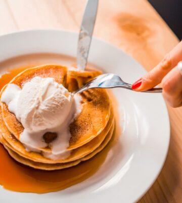 Photo shows a woman's hands as she cuts up a stack of pancakes with whipped cream and maple syrup on a plate. Bill's, a restaurant chain in the UK, is offering bottomless vegan pancakes every Friday, all day, for £5, providing customers purchase a drink. Customers have 90 minutes to eat as much as they want to.