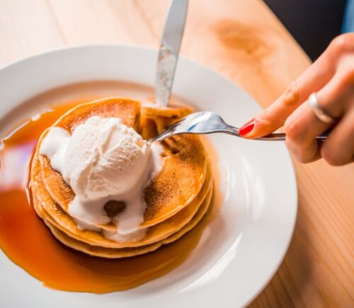 Photo shows a woman's hands as she cuts up a stack of pancakes with whipped cream and maple syrup on a plate. Bill's, a restaurant chain in the UK, is offering bottomless vegan pancakes every Friday, all day, for £5, providing customers purchase a drink. Customers have 90 minutes to eat as much as they want to.