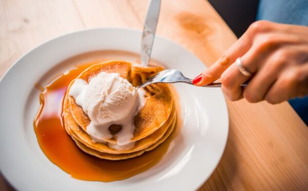 Photo shows a woman's hands as she cuts up a stack of pancakes with whipped cream and maple syrup on a plate. Bill's, a restaurant chain in the UK, is offering bottomless vegan pancakes every Friday, all day, for £5, providing customers purchase a drink. Customers have 90 minutes to eat as much as they want to.