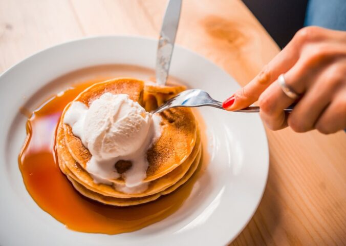 Photo shows a woman's hands as she cuts up a stack of pancakes with whipped cream and maple syrup on a plate. Bill's, a restaurant chain in the UK, is offering bottomless vegan pancakes every Friday, all day, for £5, providing customers purchase a drink. Customers have 90 minutes to eat as much as they want to.