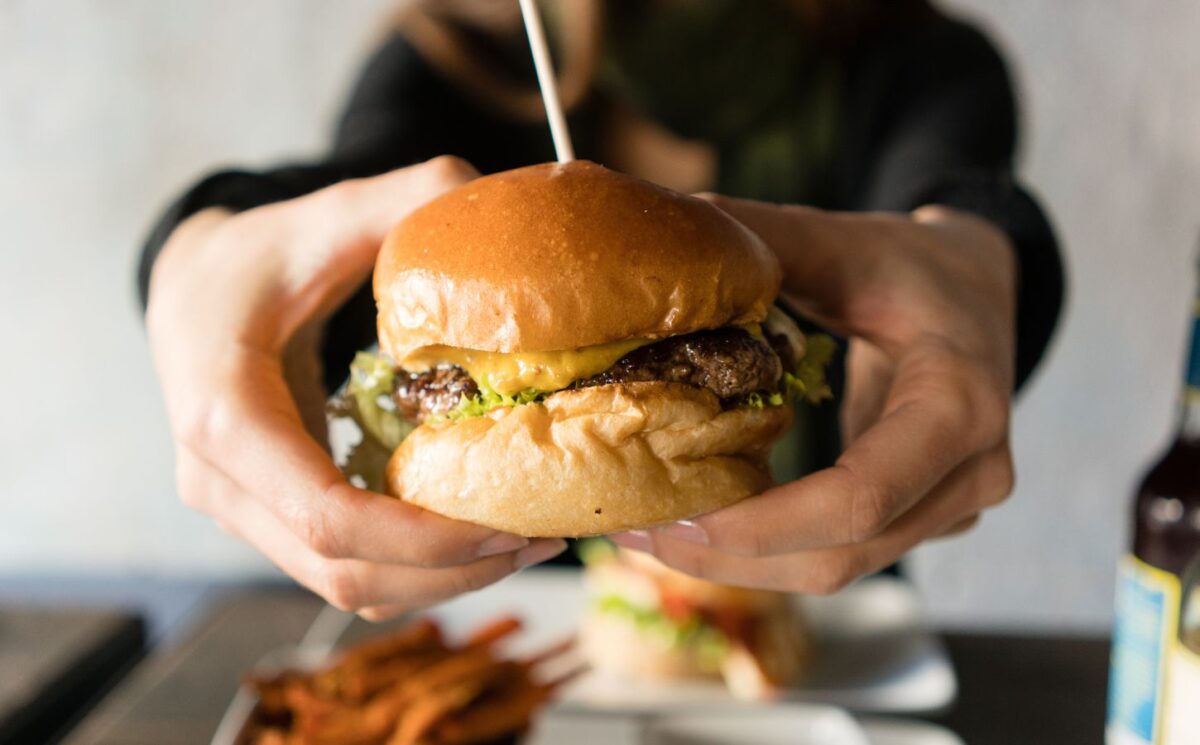 Photo shows someone's hands holding up a large beef burger with cheese. Innocent Meat has raised €6 million in its most recent fundraising round to help develop and scale its cultivated meat system, which it says is much more resource-efficient than traditional meat