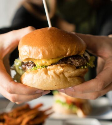 Photo shows someone's hands holding up a large beef burger with cheese. Innocent Meat has raised €6 million in its most recent fundraising round to help develop and scale its cultivated meat system, which it says is much more resource-efficient than traditional meat