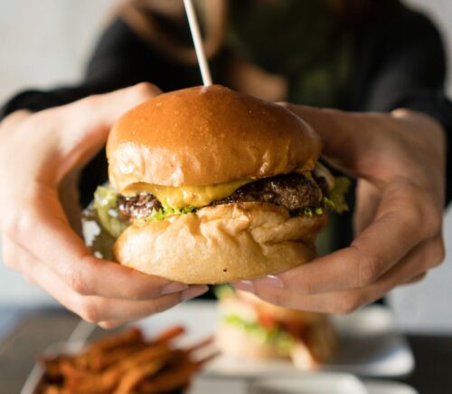 Photo shows someone's hands holding up a large beef burger with cheese. Innocent Meat has raised €6 million in its most recent fundraising round to help develop and scale its cultivated meat system, which it says is much more resource-efficient than traditional meat
