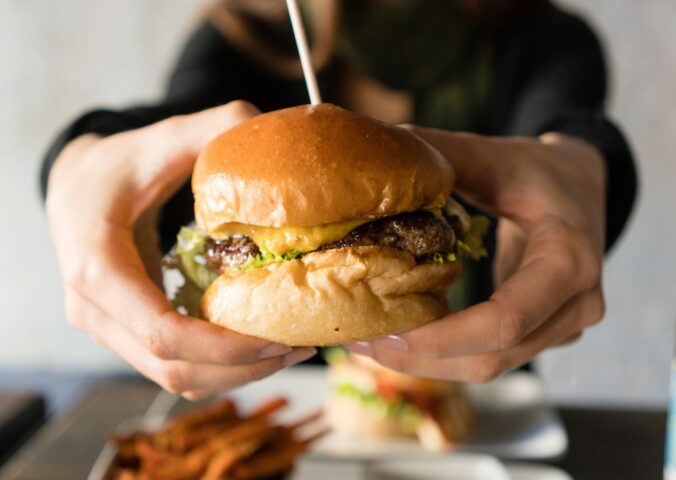 Photo shows someone's hands holding up a large beef burger with cheese. Innocent Meat has raised €6 million in its most recent fundraising round to help develop and scale its cultivated meat system, which it says is much more resource-efficient than traditional meat
