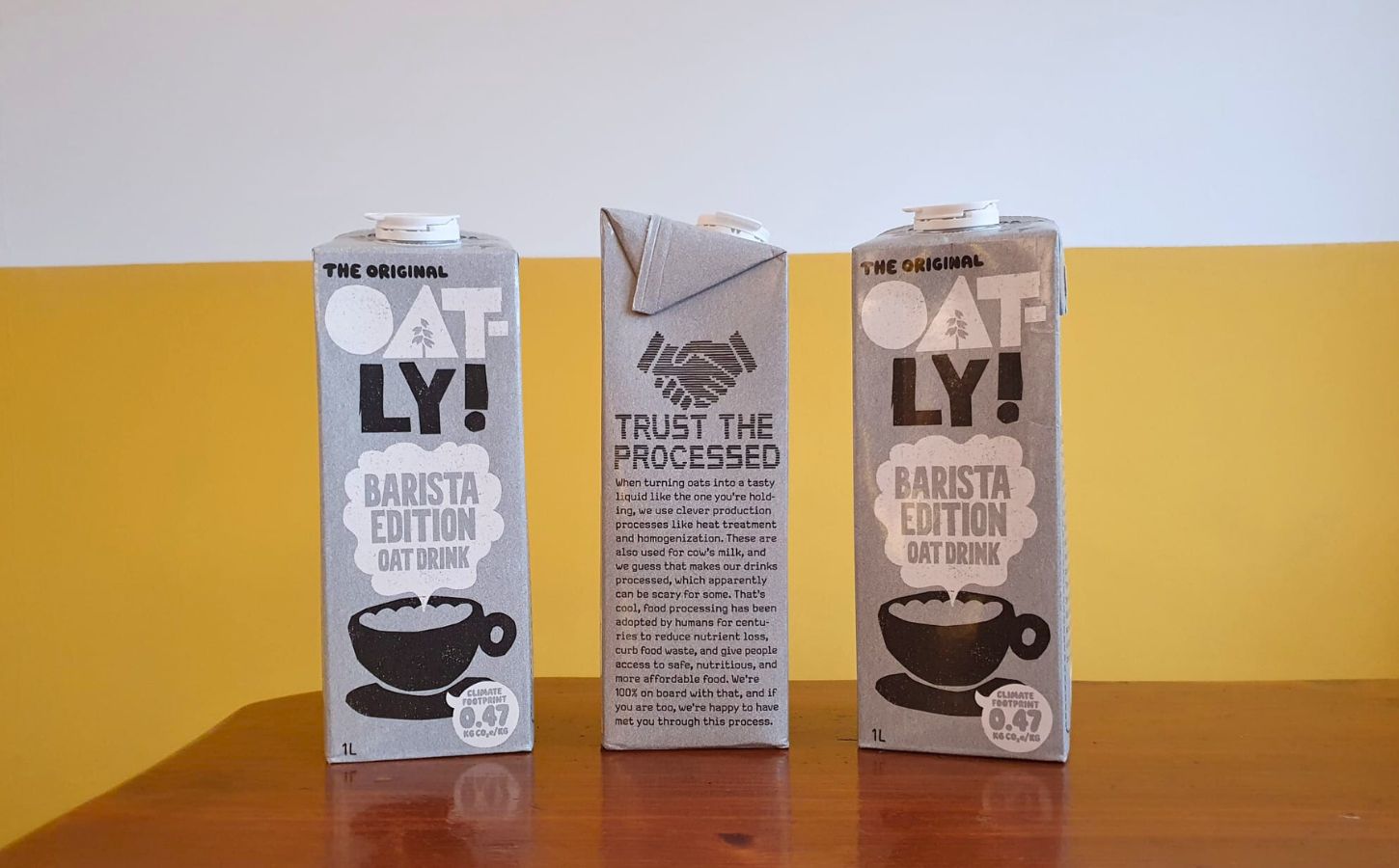Photo shows someone's hand as they hold up a carton of Oatly with the new "trust the processed" label addressing the oat milk's classification as a processed food
