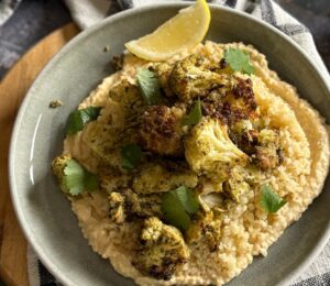 pesto cauliflower bites over grains and hummus served with lemon
