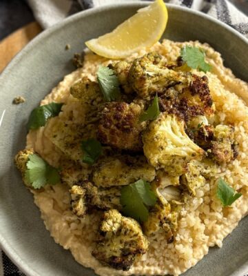pesto cauliflower bites over grains and hummus served with lemon