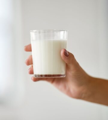 Photo shows someone's hand holding up a glass of milk. Nine people are currently experiencing “serious illness” in Idaho after drinking raw dairy milk, and two children have been hospitalized