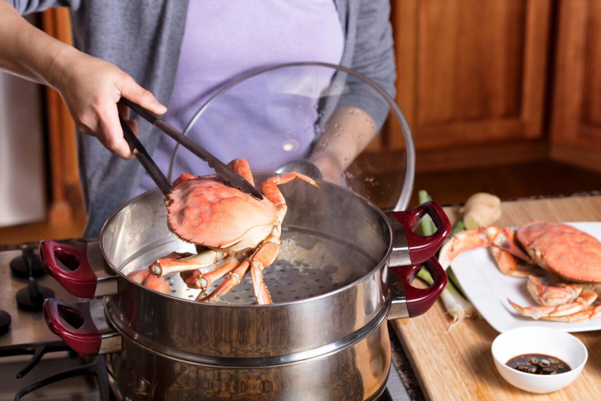 Photo shows a woman removing a dead crab from a boiling pot of water in a kitchen environment. The British government’s new animal welfare strategy says that the live boiling of crabs and other decapods is “not an acceptable killing method," but will there really be a ban?