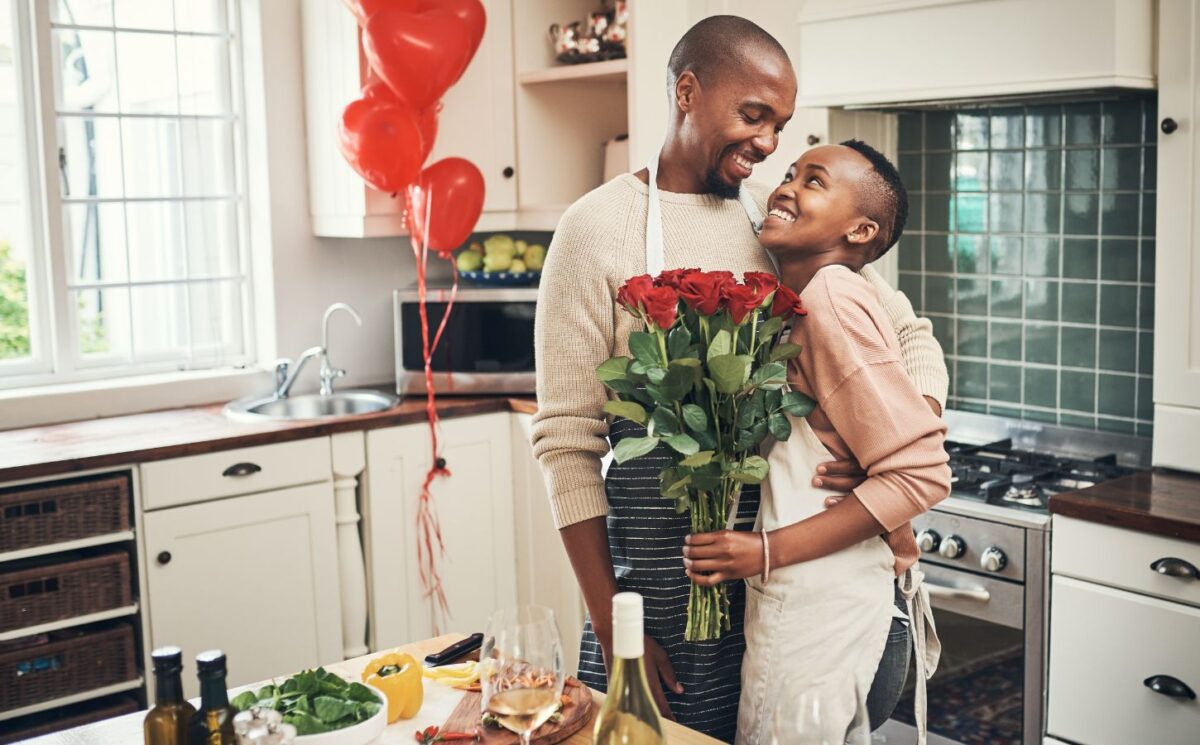 Photo shows a young couple embracing in the kitchen while cooking dinner, holding flowers, with red heart-shaped balloons in the background. Ahead of Valentine's Day, research by Redefine Meat found that nearly half of UK vegans saw dietary incompatibility as a relationship and dating dealbreaker