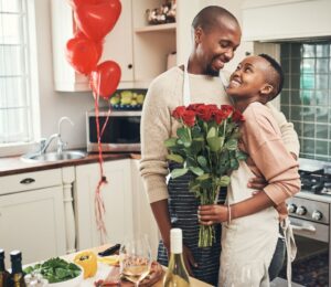 Photo shows a young couple embracing in the kitchen while cooking dinner, holding flowers, with red heart-shaped balloons in the background. Ahead of Valentine's Day, research by Redefine Meat found that nearly half of UK vegans saw dietary incompatibility as a relationship and dating dealbreaker