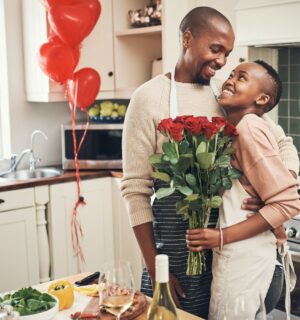 Photo shows a young couple embracing in the kitchen while cooking dinner, holding flowers, with red heart-shaped balloons in the background. Ahead of Valentine's Day, research by Redefine Meat found that nearly half of UK vegans saw dietary incompatibility as a relationship and dating dealbreaker