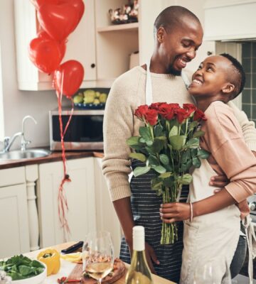 Photo shows a young couple embracing in the kitchen while cooking dinner, holding flowers, with red heart-shaped balloons in the background. Ahead of Valentine's Day, research by Redefine Meat found that nearly half of UK vegans saw dietary incompatibility as a relationship and dating dealbreaker