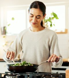 Photo shows a young woman cooking vegetables in a wok in her kitchen while reading a recipe on her phone. Around 30 million people reportedly participated in this year's "record-breaking" Veganuary 2026 campaign.