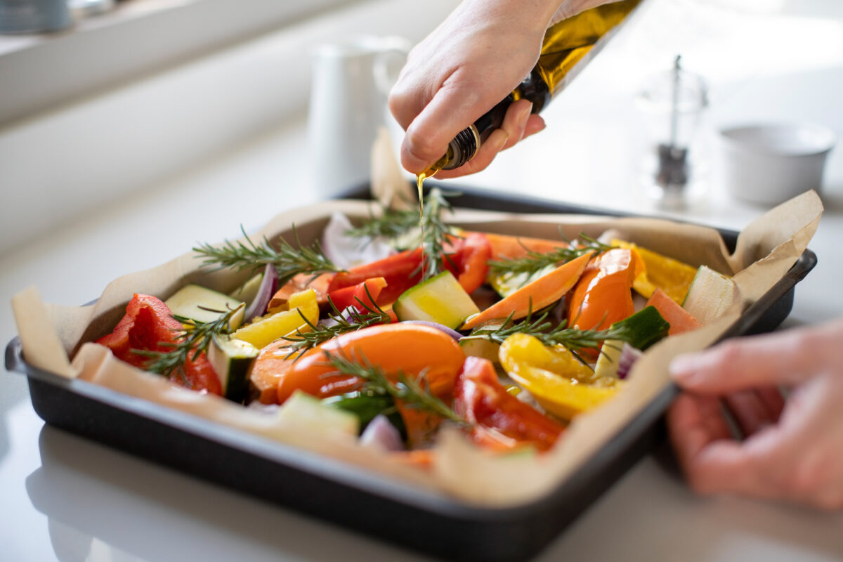 Photo shows someone's hands as the season chopped vegetables and herbs in a baking tray